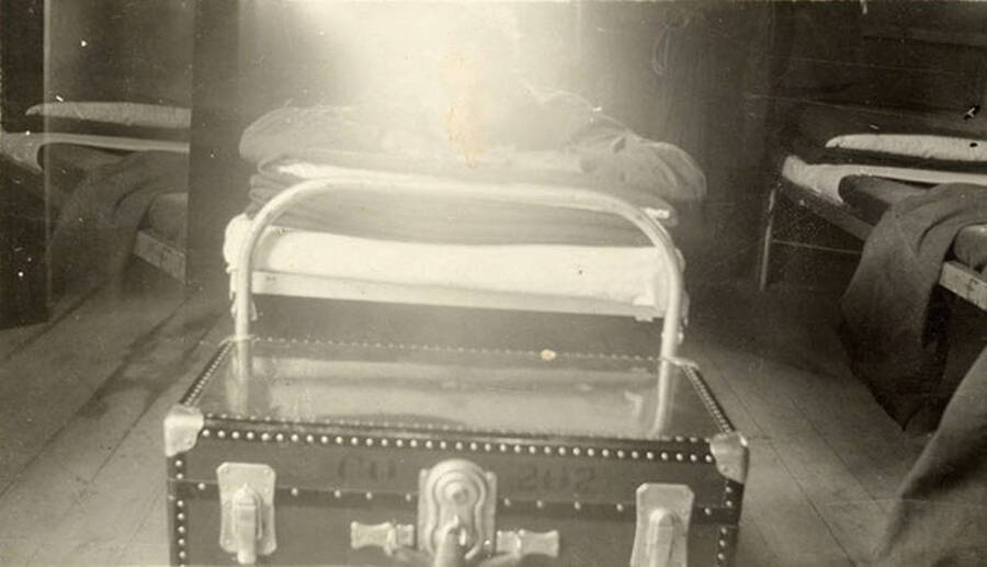 Close-up photo of a bed and trunk inside a barracks. The trunk reads: 'CO 202'.