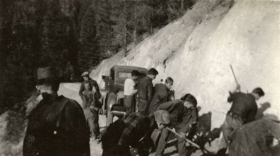 Several CCC men working on a road, many holding hand tools, with a truck parked in the background. Writing below the photo reads: 'Super-Crew'.