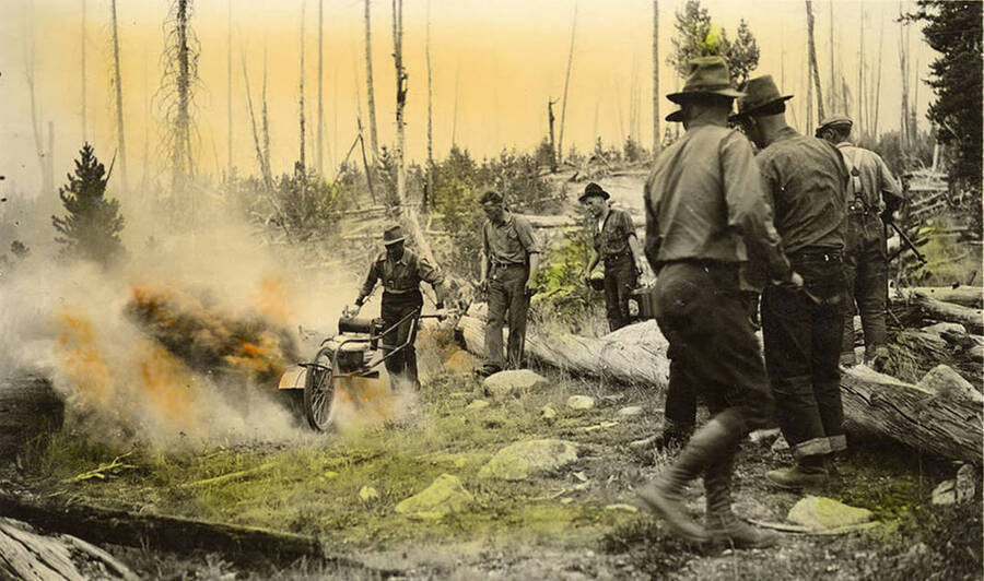 One man uses a cycle machine to set a fire line while several CCC men watch. The photo is tinted. Writing below the photo reads: 'Fire'.