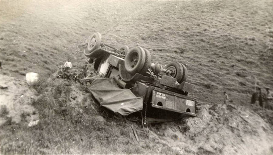 Photo of an overturned truck with CCC men looking on. Writing underneath each photo is one word that makes the sentence: 'This truck overturned by accident' Word on this image is: 'This'.