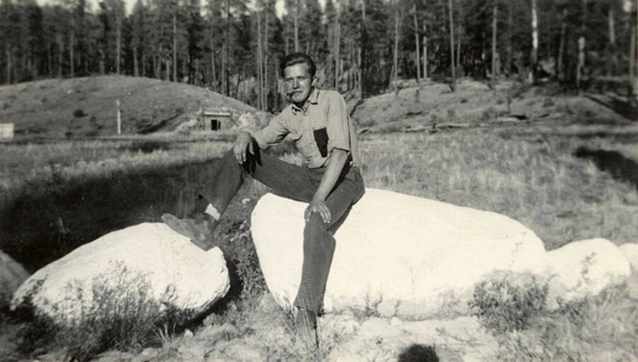 Portrait of a CCC man 'Tex', posed on a rock with a cigar in his mouth. Writing under the photo reads: 'Tex'.