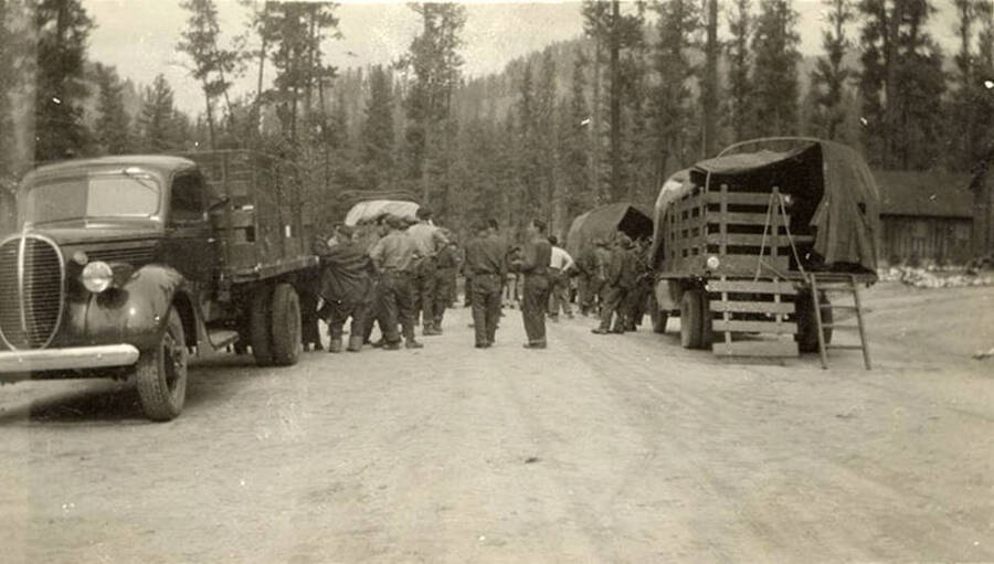 CCC crew getting ready to head to the work site, standing in the road around 4 trucks with open beds. Writing below the photo reads: 'Work call'.