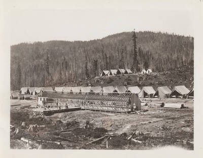 Construction of a building frame is underway  at a CCC tent camp.
