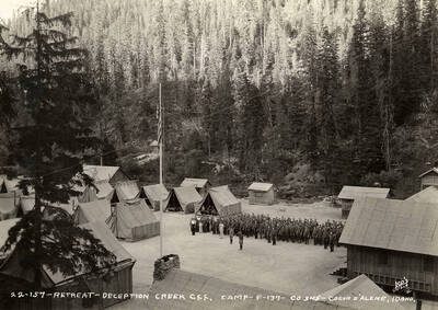 Uniformed CCC men standing at attention during retreat at Deception Creek CCC Camp. Writing on the photo reads: ' Retreat Deception Creek CCC Camp F-137 Company 545 Coeur d'Alene, Idaho Leo's Studio'.