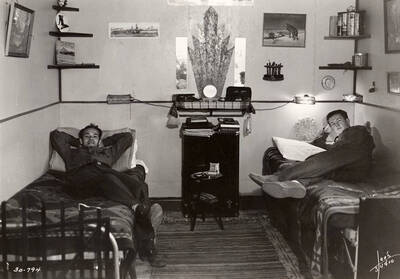 Two CCC men lounging in their dorm room at Four Corners CCC Camp, F-164.  Writing on the photo reads: 'Leo's Studio'. Back of photo reads: 'Four Corners Priest River Kaniksu, National Forest'.