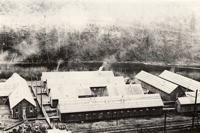 View of CCC camp F-120 near Avery, Idaho and the St. Joe River behind. The sign reads: 'CCC Camp F-120'. Back of photo reads: 'CCC Camp F-120 Avery 1933'.
