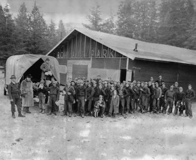 Frank Bruce Robinson with CCC men at Rowland Park building near Robinson Lake Park. Building is labeled 'Rowland Park' and the writing on the back of the photo reads: '1-10-59 Robinson (in black hat) distributes coffee and sandwiches to CCC workers on Park he donated to County. Old Rowland Park Building next to Robinson Lake Park. 1st person on far left may be Fred Horning, next person is FBR [Frank Bruce Robinson] and W.T. [William] Marineau is standing on back of truck. Circa late 30's'.