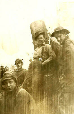 Four CCC men posing for a photo, leaning up against a tree stump.