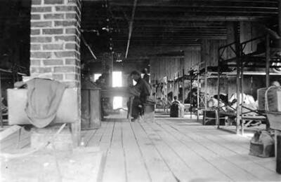 CCC men sitting at a table in in a CCC bunkhouse in Headquarters, Idaho. Writing below the photo reads: 'Bunk H(ouse) Headquarters'.