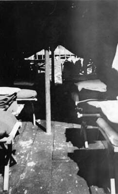 An interior view of a tent in a CCC camp. There are at least six cots in the tent with folded blankets on the end. Writing under the photo reads: 'Inside Tent 3 Idaho'