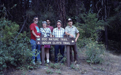 Five people standing behind a sign for the Indian Cliffs trailhead. One of the men is wearing a forest ranger's uniform. The sign reads: 'CCC Nature Trail, Indian Cliffs Trail'.