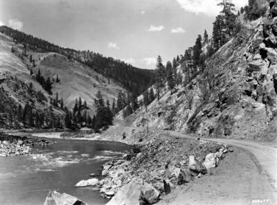 A dirt road meanders along a river at the bottom of a valley.