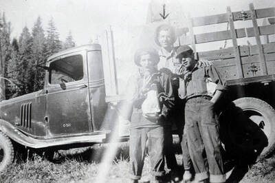 Three CCC enrollees posing in front of truck. Two of the men are pretending to eat food and the last man (standing in the center) has an arrow drawn over his head. The door of the truck has a mark that reads: 'C-511'.