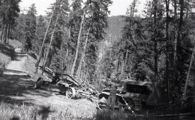 On a steep mountain road a bulldozer is pulling a road grader (possibly it was stuck?). The photo may have been taken on Magruder Corridor road.