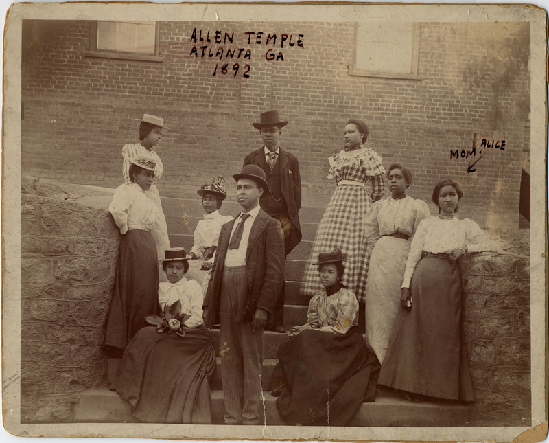Sepia photo of Alice Anthony Cheatham (1876-1959) and family. Seven people stand and three people sit on steps leading to the brick building behind them. They are all dressed in formal wear and none are looking at the camera. Alice is the rightmost figure, wearing a light-colored blouse, belt, and long skirt. In marker is written "ALLEN TEMPLE ATLANTA GA 1892" on the top center, and an arrow pointing to Alice with "ALICE MOM" written above her. The photo is pasted on a cardboard backing. On the back of the cardboard is written "Allen Temple Atlanta 1892" in pencil and black marker. Alice, who was "part Indian, mixed with Oriental" (I Guess I'll Get the Papers and Go Home Advance pg 1), worked as a maid and schoolteacher in Tennessee.