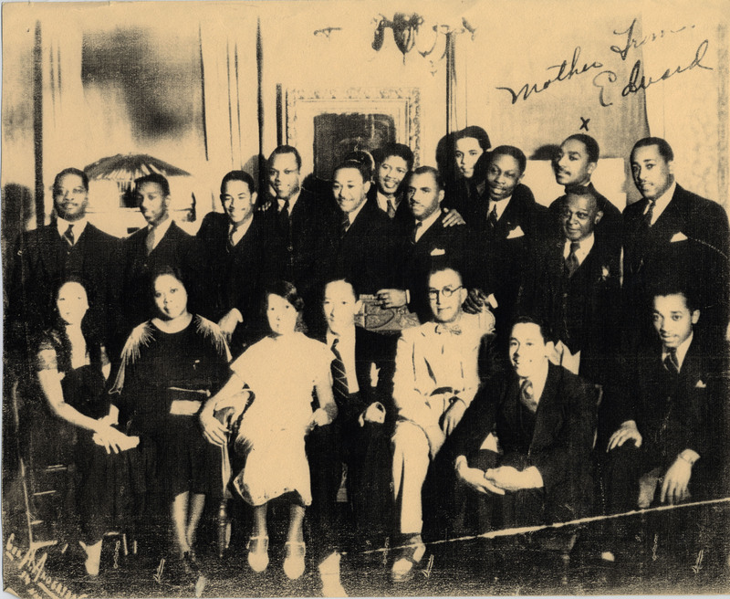 Doc Cheatham (center) sits on a chair between his mother, Alice L. Anthony Cheatham (1876-1959) on the left, and father Marshall Nye Cheatham (1869-1942) on the right. To Marshall Cheatham's right is his first son and Doc's older brother, Marshall Cheatham Jr. (1903-1978). Around them are other family members. On the top right is cursive is written: "Mother from Edward." On the bottom left is "Gus Anderson '34." The picture has four small holes poked through the corners, such as those made by thumbtacks.