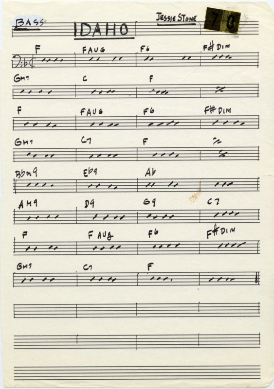 Loose page with printed music staves. At the top, "Bass," "Idaho," and "Jessie Stone," are written and underlined in black marker. In the top right corner are "7" and "0" gold reflective stickers. Written in black marker are dashes to indicate eighth notes, repeat measure signs,and chord names over measures. Measure lines, the key signature (Bb) and time signature (cut time) are written in black pen. There is a small, light brown mark like a scratch near the middle of the page. "Idaho" (1947) was composed by Jesse Stone (1901-1999). Cheatham and Nicholas Payton (1973-) recorded but never released this piece.