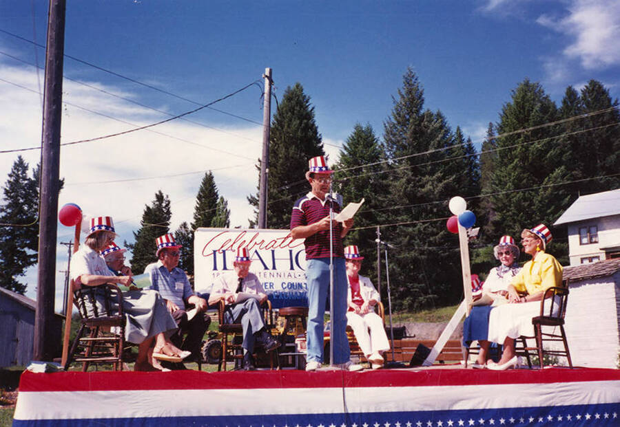 Gary Eggers, Bovill's mayor, speaking on stage during Statehood Day celebration. Behind him are (l to r): Mary Reed of Moscow; Norma Dobler, featured speaker and former representative and senator; Jerry Brown, mayor of Kendrick; Harold Freeman, Juliaetta mayor; Marie Vogel, Troy mayor; Marie Scharnhorst, Genesee rep; Carol Reynolds, Potlatch rep.