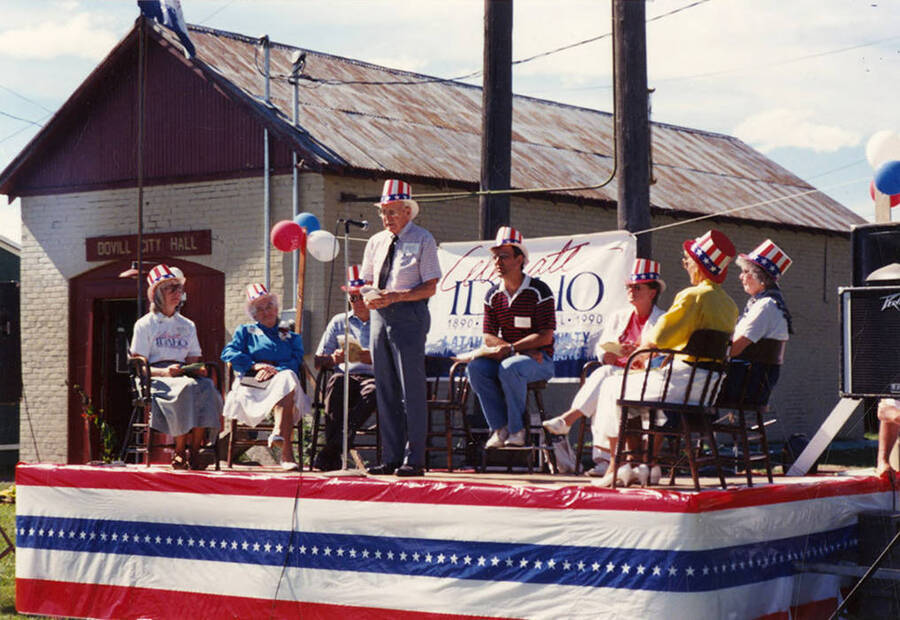 Harold Freeman, Juliaetta's mayor, speaking on stage during Bovill's Statehood Day celebration. Behind him are (l to r): Mary Reed of Moscow; Norma Dobler, featured speaker and former representative and senator; Jerry Brown, mayor of Kendrick; Gary Egger, Bovill mayor; Marie Vogel, Troy mayor; Marie Scharnhorst, Genesee rep; Carol Reynolds, Potlatch rep.