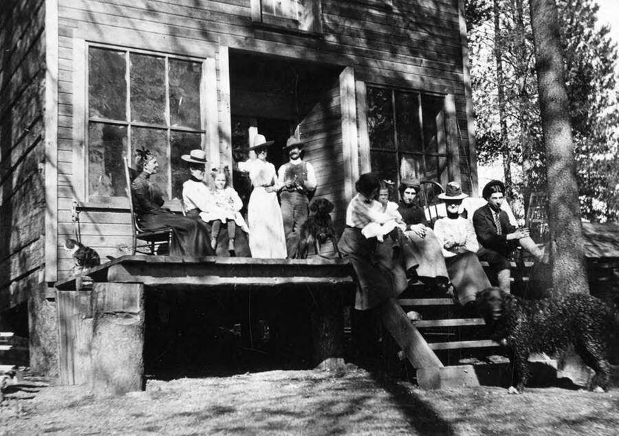 Mr. and Mrs. Bovill, their girls, some guests, and some pets sit on the front porch of their store.