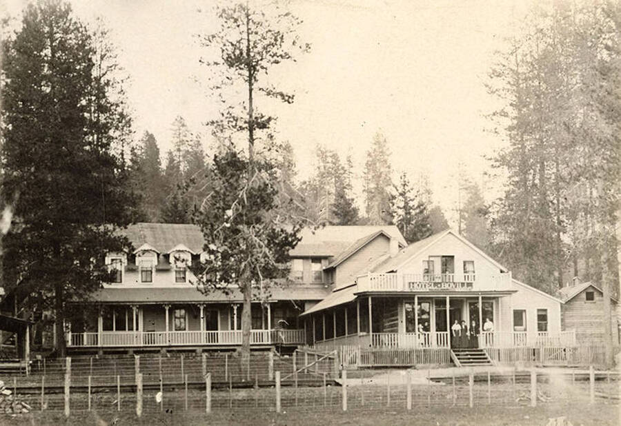 Women stand on the front porch of the Bovill Hotel, surrounded by trees.
