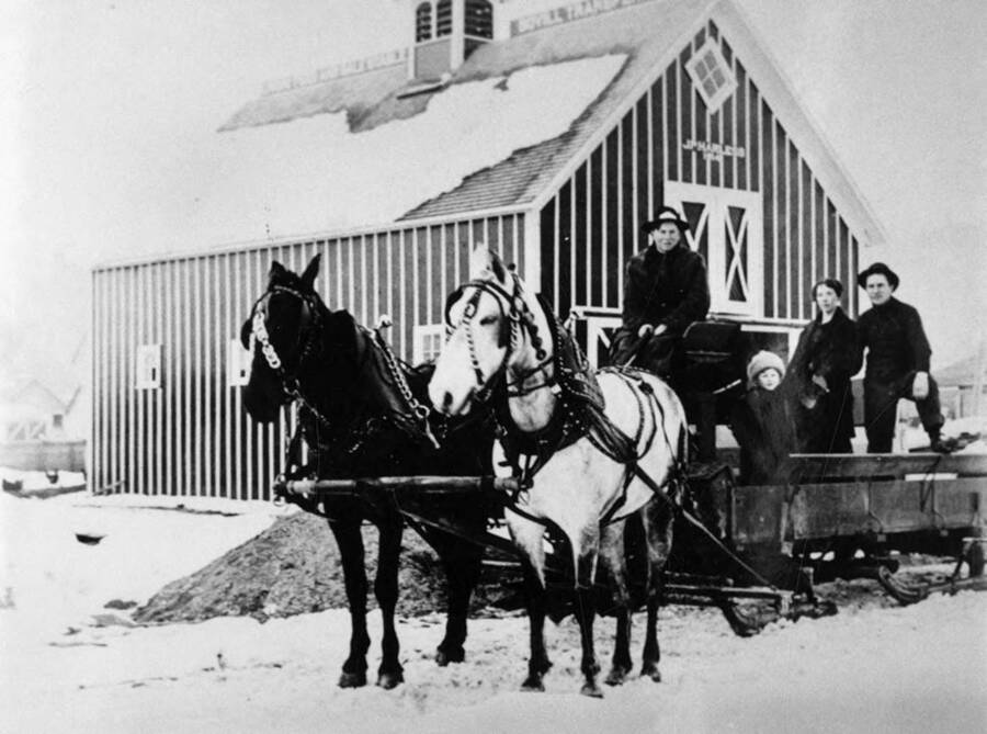 Horses pulling a carriage with a family on it outside the J.P. Harless Livery Stable.