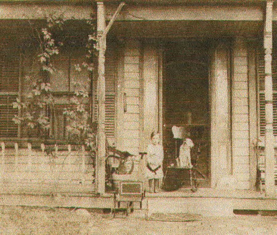A Bovill house with a child and a dog sitting on the front porch.
