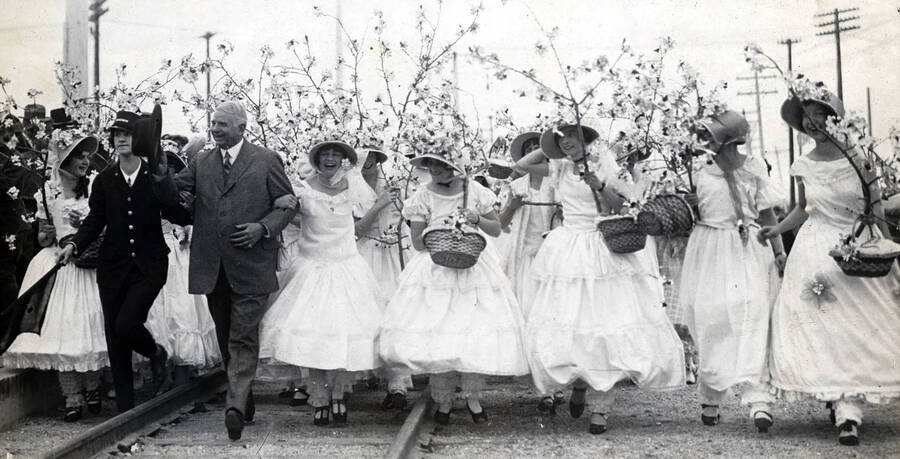 Brakeman' Rose Regan and Caroline Athey, Apple Blossom girl, leading U.P. President Carl R. Gray down platform. Celebration of coming of Union Pacific main line to Boise. Boise, Idaho.
