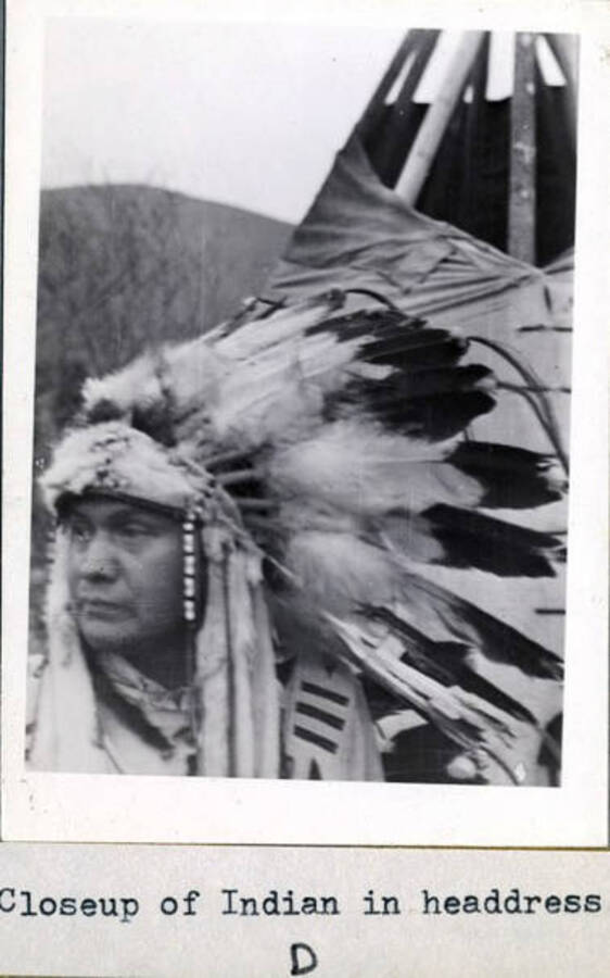 Rev. Stephens Reubens speaking, Indian in headdress in front of tepee