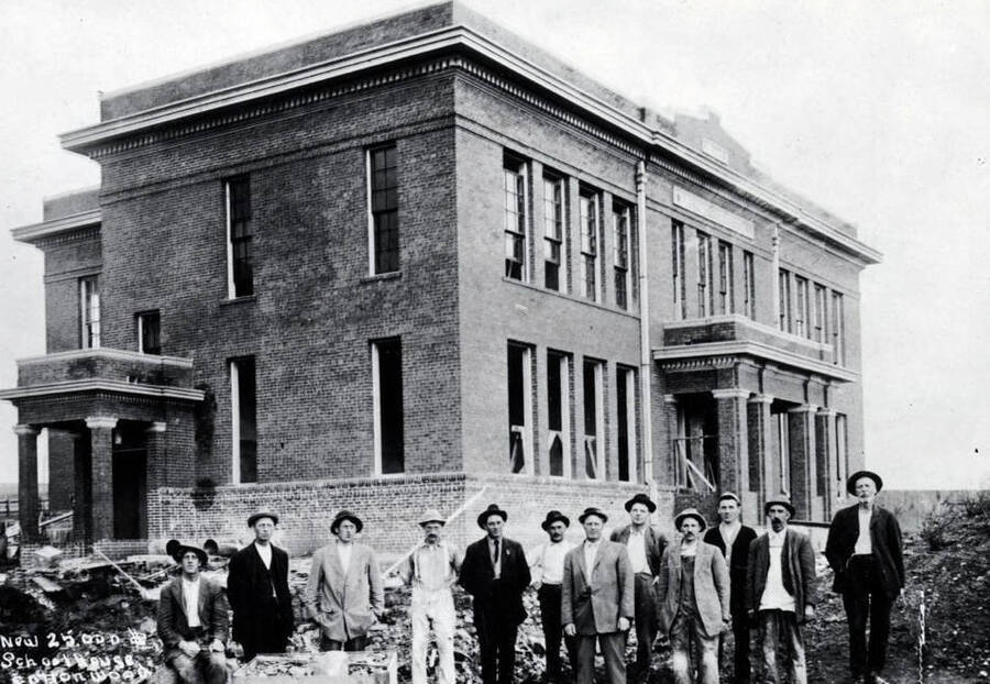 Twelve men posed outside building