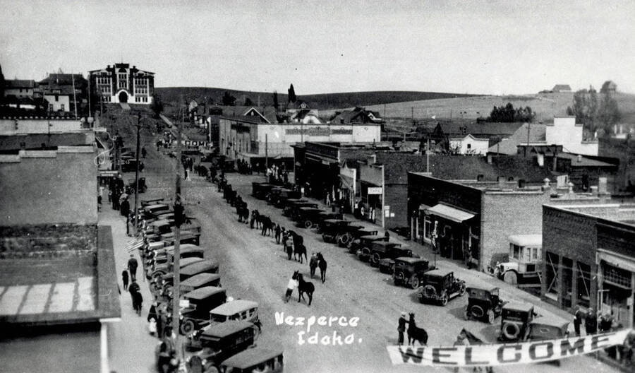 Street scene with horses, men and cars lined up [parade?]. Nez Perce, Idaho.