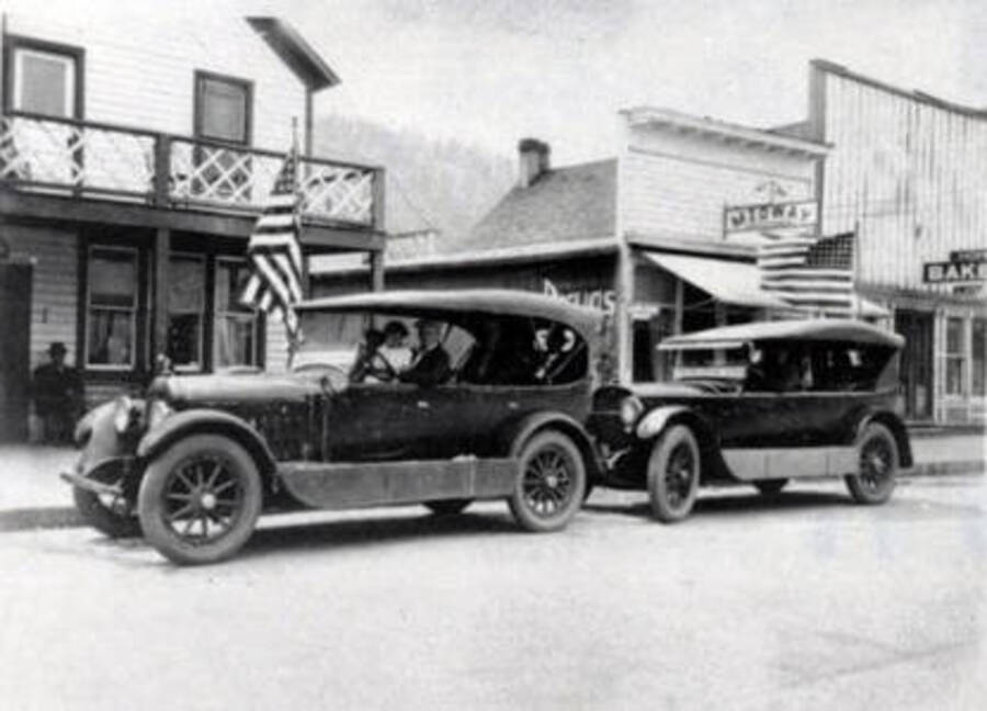 View of two cars parked on street. Buildings partially shown are Midway and a bakery. Orofino, Idaho.