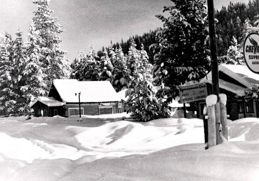 Winter scene. View of a home and portion of a building with sign 'Sportsman's Club, Beer, Pop, Coffee, Lunches.'
