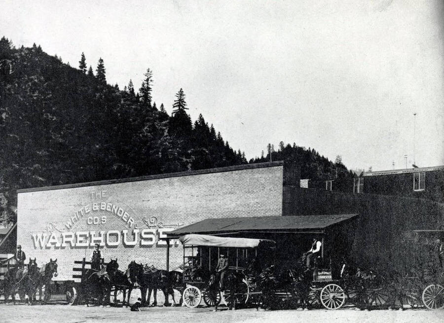 Horse-drawn delivery wagons of George K. Garrett Transfer and Coal beside the White & Bender Co.'s Warehouse. Wallace, Idaho.
