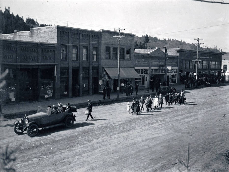 Group of people walking down Main Street behind a car
