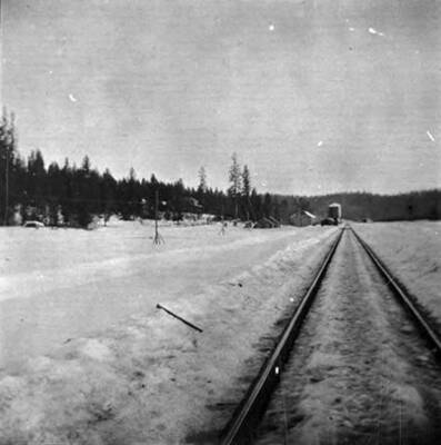 Railroad tracks with water tank and warehouse in the distance.