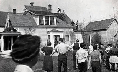 Firemen on the roof of a house. Group of people watching. Wallace, Idaho.