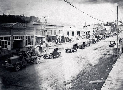 Long line of cars and trucks going down Main Street. Flags displayed