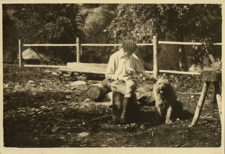 Thelma Page, faced away, sit on a log stump and pets a dog to her left.