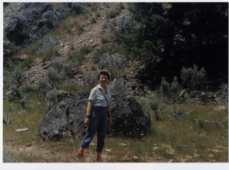 Dorothy Taylor stands in front of a rocky hill with shrubs.