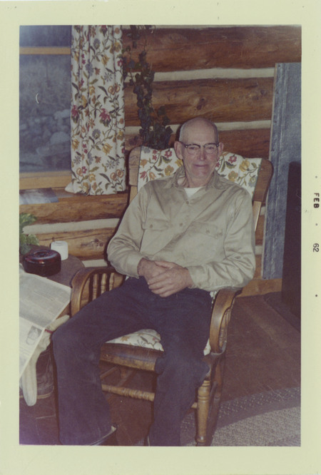 Jess Taylor sits on a floral-patterned chair, in a log cabin.