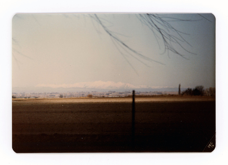 The front of a postcard decorated with a picture of a mountain range in the distance.