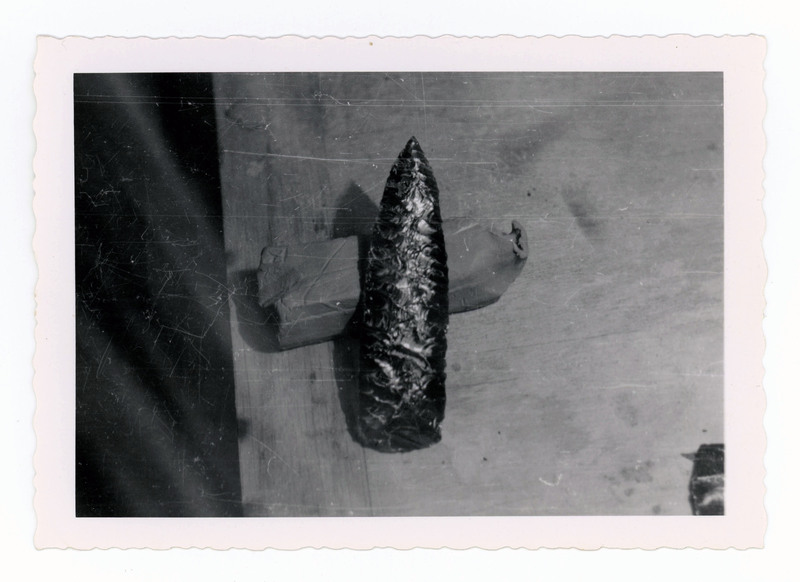 A printed picture of a lithic point resting on a piece of clay.