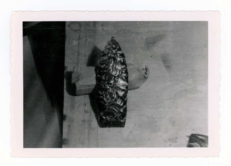 A printed picture of a lithic point resting on a piece of clay.