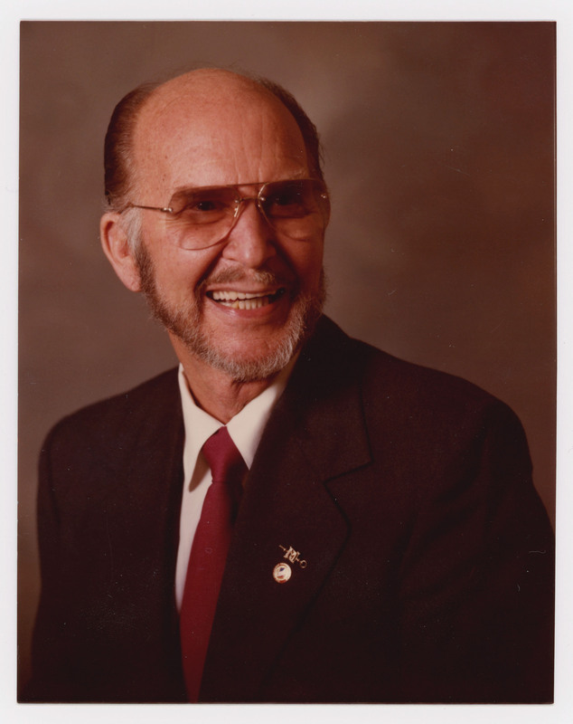 A photo of Donald Crabtree in a suit smiling for a headshot. He is wearing pins on his suit.