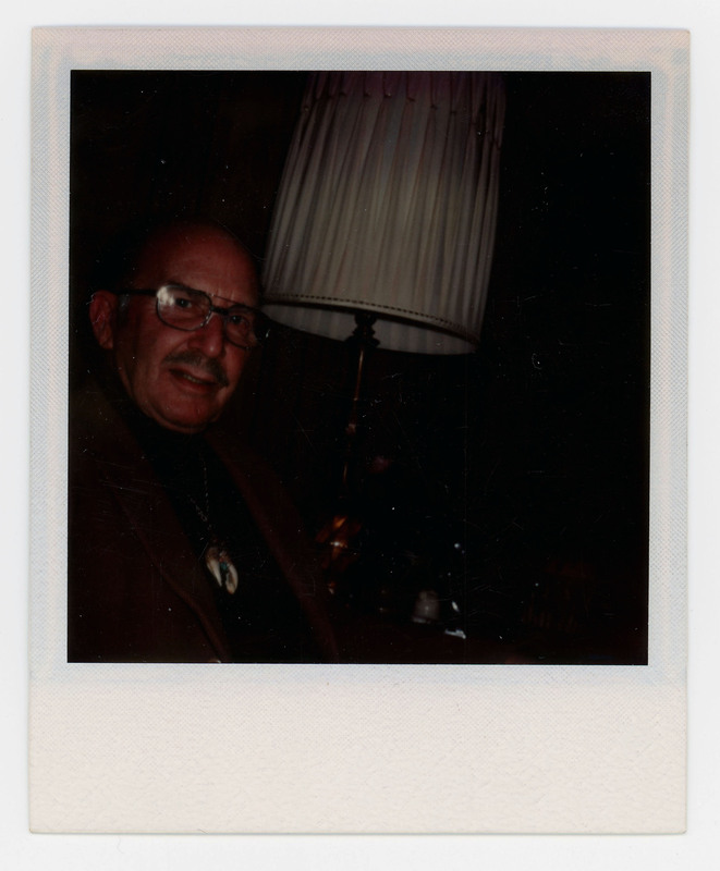 A photo of a man in a dark room sitting next to a white lamp.