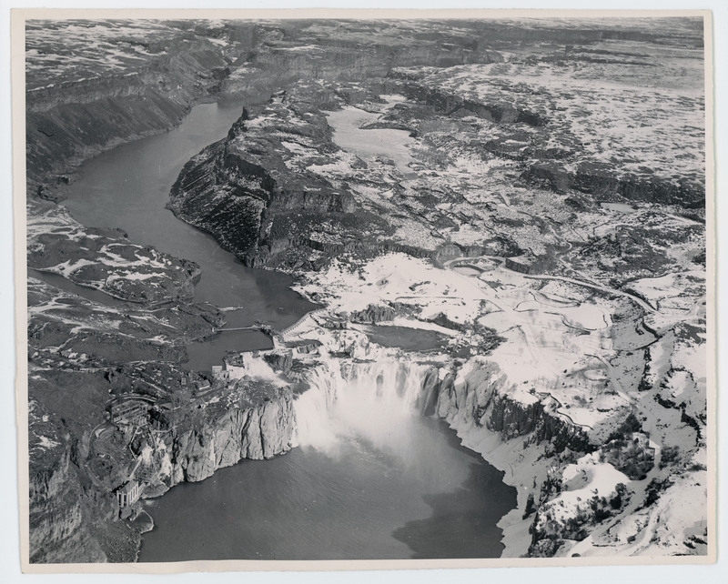 An aerial view of a river with a large waterfall. The mountains are covered in snow. This is Shoshone Falls in Twin Falls.