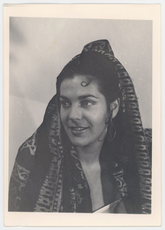 A photo of a woman wearing a patterned scarf over her head. Her hair is done up, and she is wearing jewelry. She is not looking at the camera.