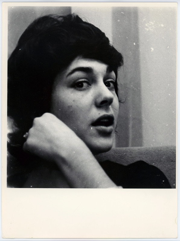 A photo of a woman with dark hair giving side eye to the camera. The image is just of her head and her hand is by her cheek.