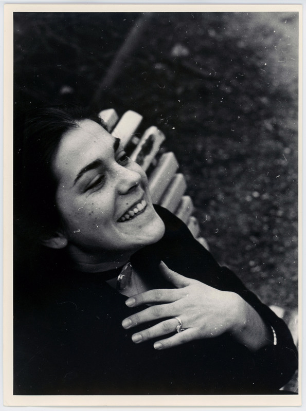 A photo of a woman sitting on a bench laughing while looking at the sky. Her hand is over her heart.